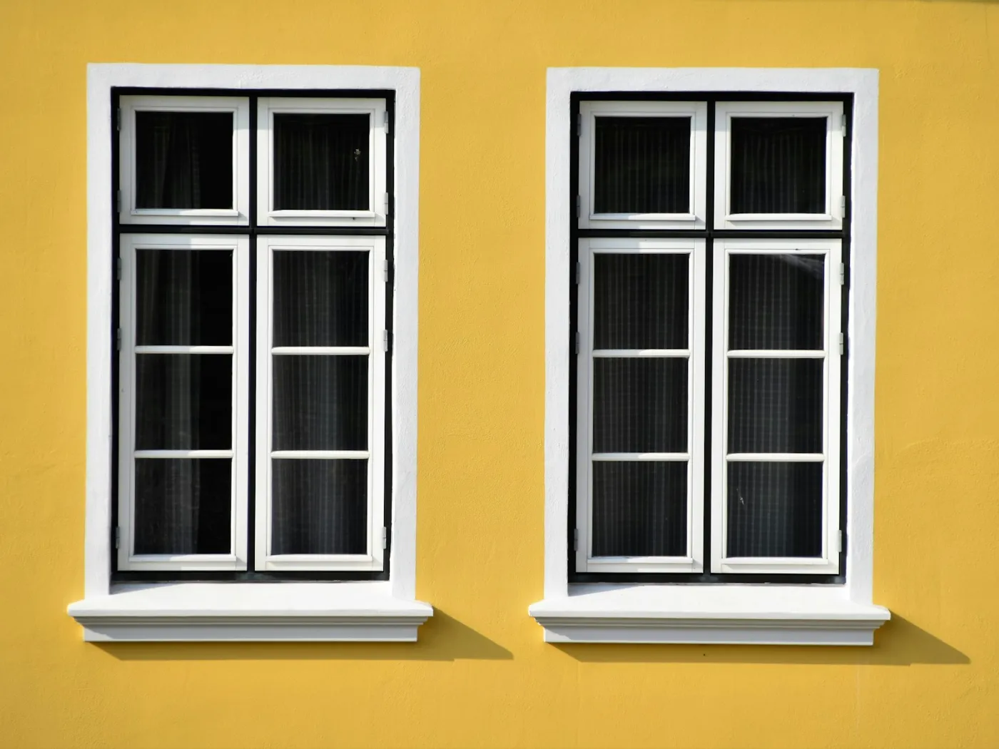 Deux fenêtres blanches à petits bois et appuis neufs sur une façade jaune